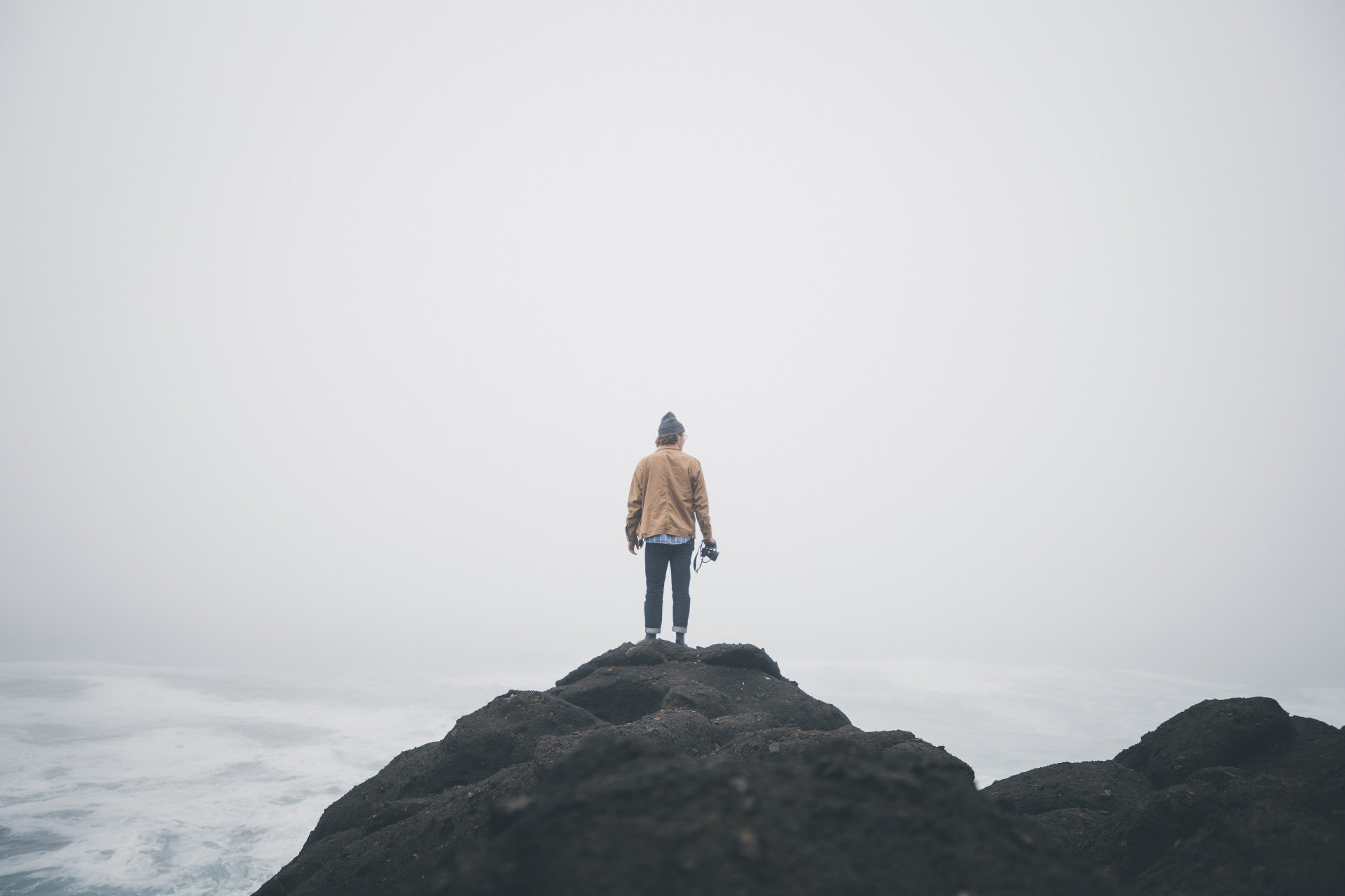 A man stands on a rocky mountain under a white sky.